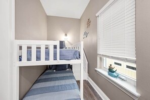 Ein Kinderstockbett mit Blick aus dem Fenster, einer an der Wand montierten Lampe und einem kleinen Regal mit Dekoration.