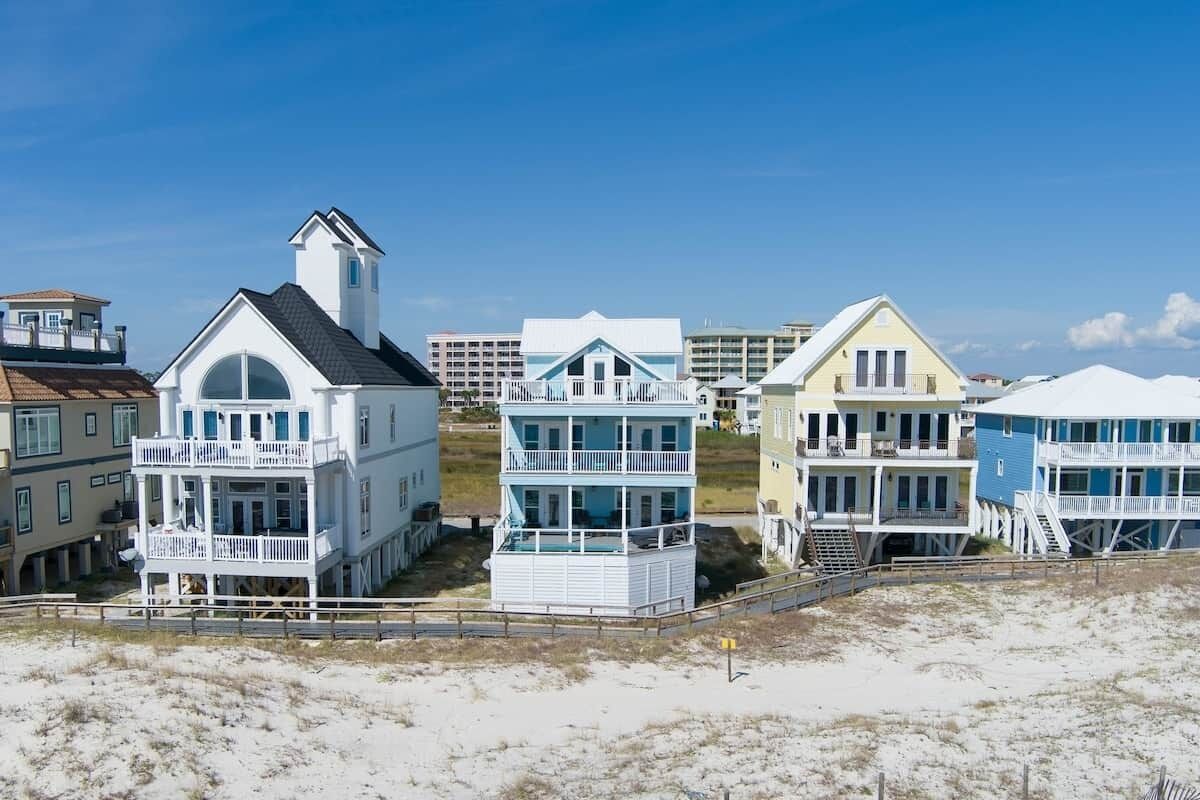 A beachfront property with multiple-story buildings, including a prominent white building with a balcony and a blue building with a balcony.