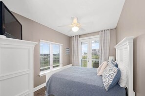 A bedroom with a bed, a ceiling fan, a window with blinds, and a view of a building outside. - Eden's Waters: Gulf Front; Htd Prv Pool; Golf; Arcade; Lux Services; Strlnk; (Baldwin County)