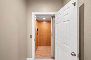 A hallway leading to a wooden door with a white frame, a doorknob, and a doorbell. - Eden's Waters: Gulf Front; Htd Prv Pool; Golf; Arcade; Lux Services; Strlnk; (Baldwin County)