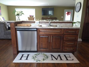 A kitchen with a built-in dishwasher, wooden cabinets, a granite countertop, and a 'HOME' mat on the floor.