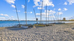 A sandy beach with several boats moored on the shore, a clear blue sky, and a distant building. - Sail Bay Oasis • Steps to Sand & Boardwalk (San Diego)
