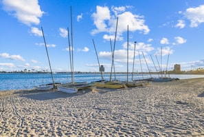 A sandy beach with several boats moored on the shore, a clear blue sky, and a distant building. - Sail Bay Oasis • Steps to Sand & Boardwalk (San Diego)
