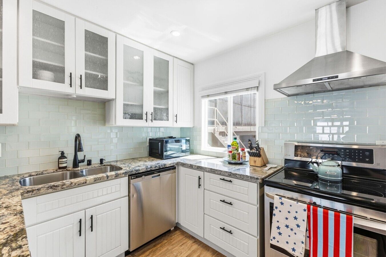 Una cocina con armarios blancos, lavavajillas, microondas, estufa y ventana con vistas.