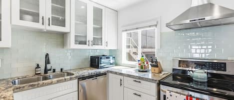 A kitchen with white cabinets, a dishwasher, a microwave, a stove, and a window with a view.