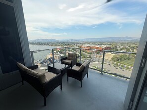 En balkon med fletningsmøbler, udsigt over en by og et vandområde.
