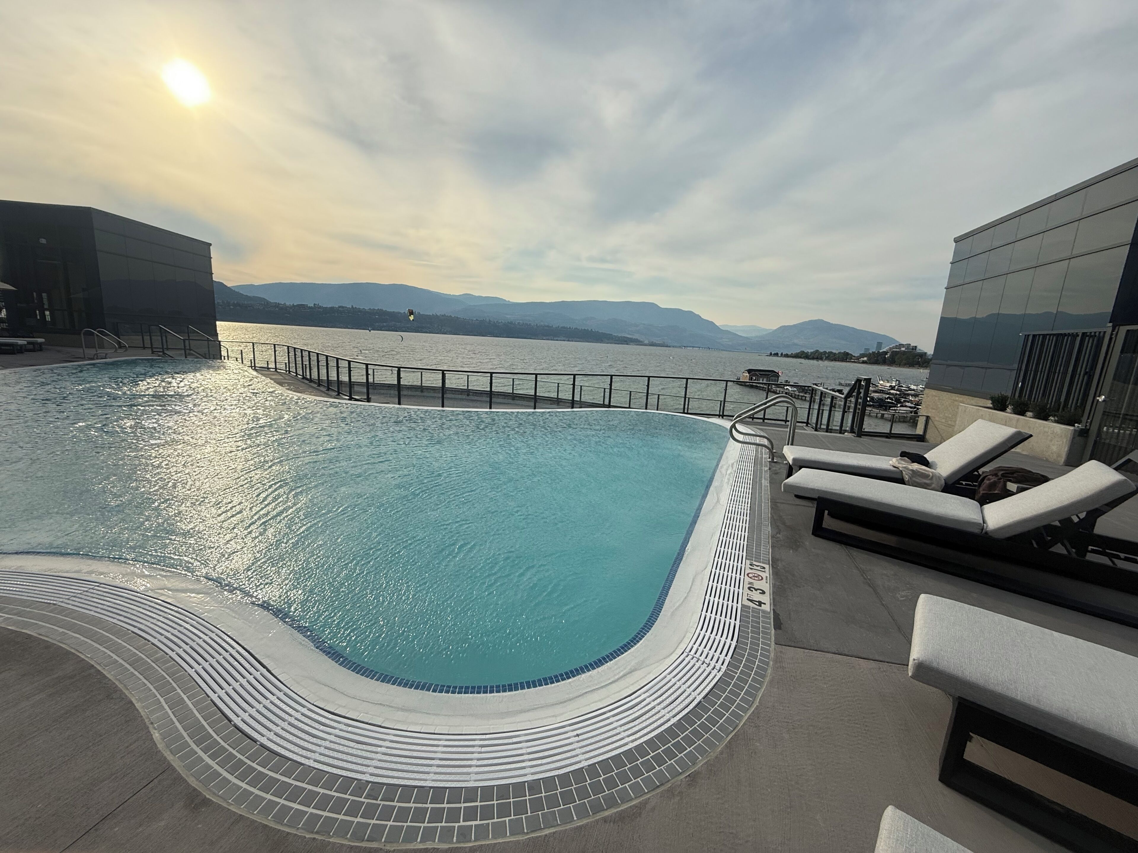 A swimming pool with a curved edge, lounge chairs, and a view of a body of water with mountains in the distance.