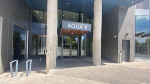 Ein moderner Gebäudeeingang mit einem Schild, auf dem 'AQUA II' steht, und einer Glastür.