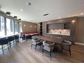 Et moderne interiør med et centralt spisebord omgivet af stole, et køkken med marmorbeklædt bagvæg og et siddeområde med en rød bænk.
