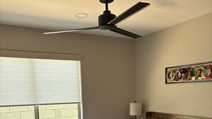 Een slaapkamer met een bed, plafondventilator, raam en een lamp aan de muur.