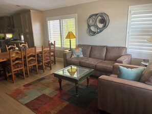 A living room with a sofa, a coffee table, a dining area with chairs, and a kitchen in the background. - Winter in AZ!! Early bird pricing!! 1000.00 DOLLARS OFF for any 2 month stay!! (Scottsdale)
