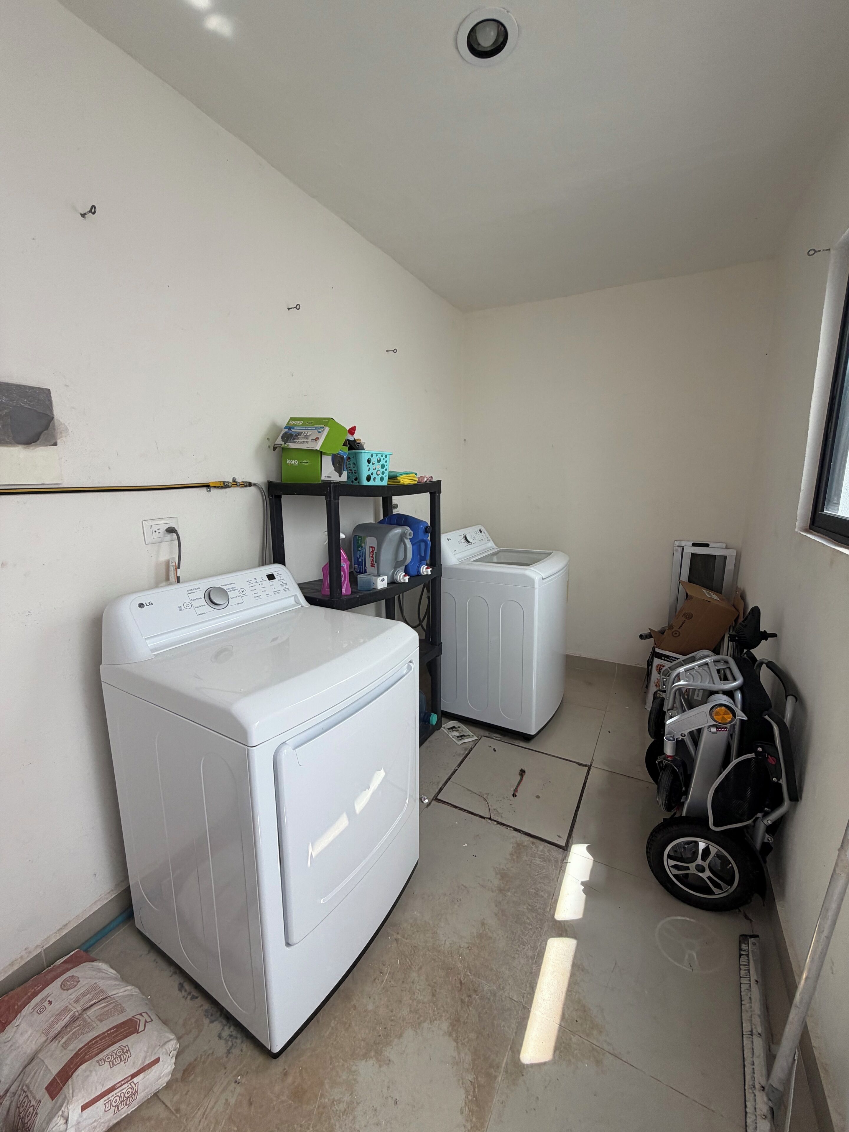 A laundry room with a front-loading washer and dryer, a small shelf with cleaning supplies, and a window.