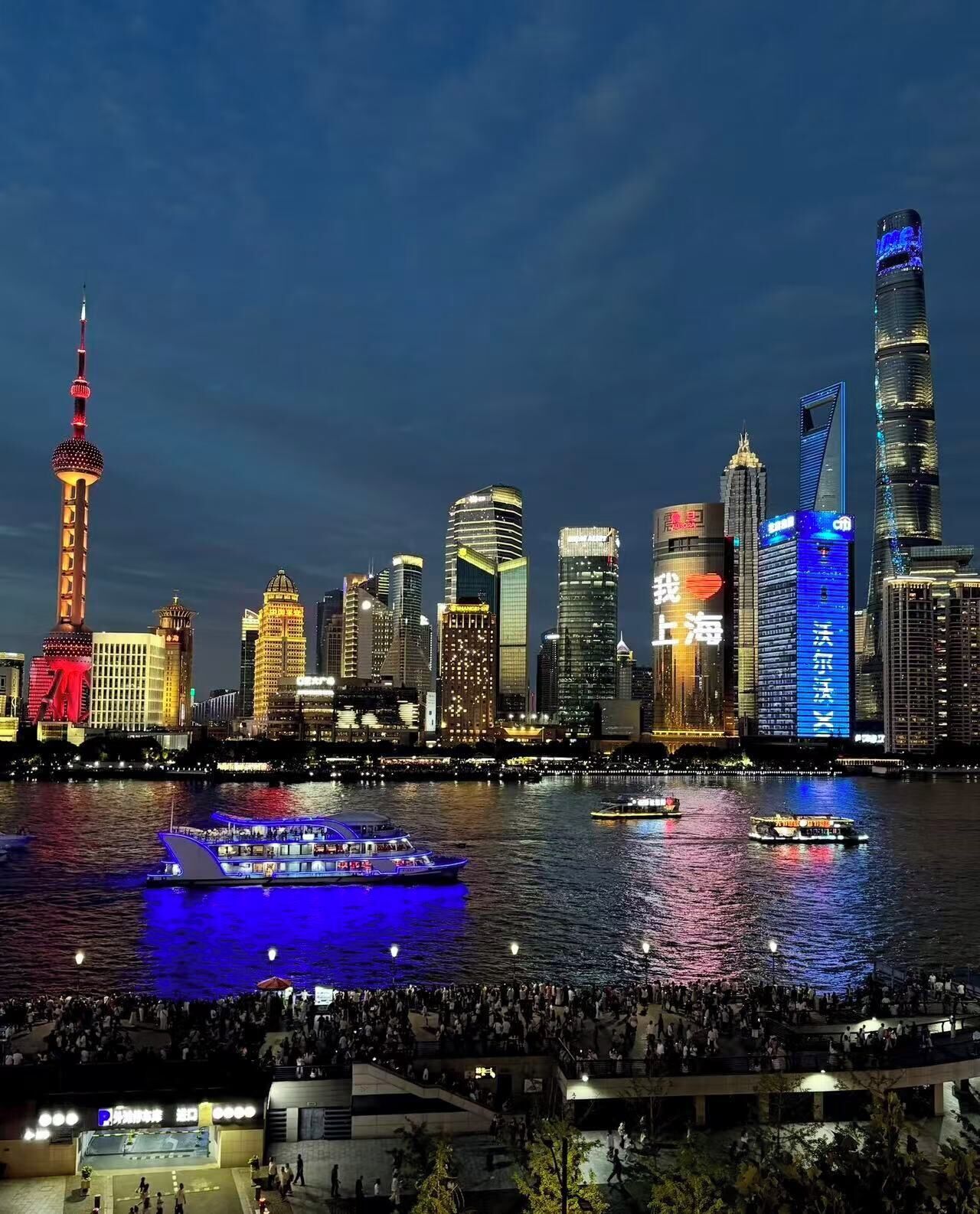 A city skyline with illuminated buildings and a river with boats.