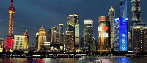 A city skyline with illuminated buildings and a river with boats.