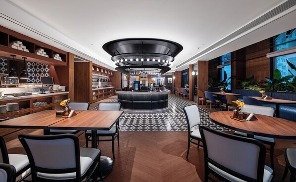 A modern hotel lobby with a central bar, seating areas, and a patterned floor.