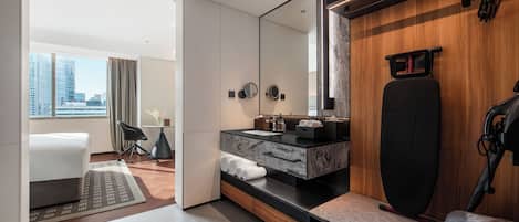 A modern hotel room with a large mirror, a workout station, a desk, and a view of the city.