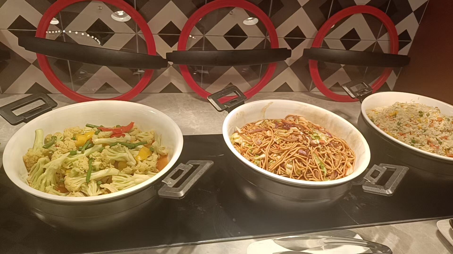 Een buffettafel met drie bakken vol eten, een broodrooster en een magnetron.