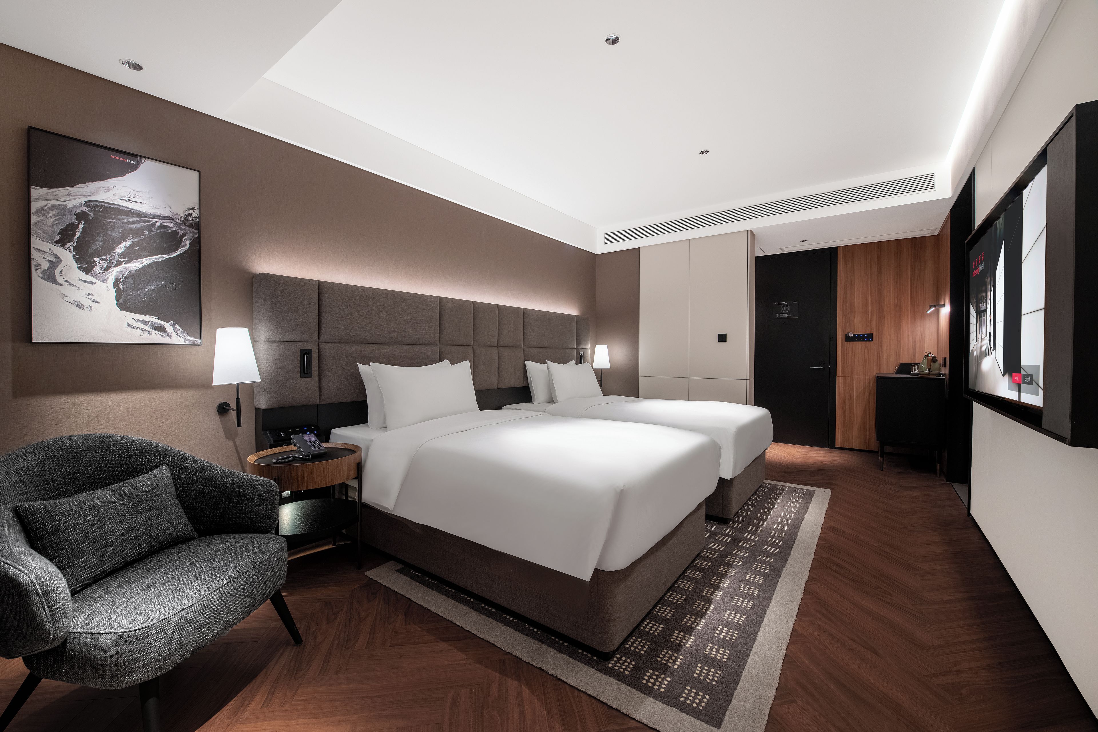 A modern hotel room with a large bed, a seating area with a chair, and a desk with a lamp.