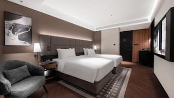 A modern hotel room with a large bed, a seating area with a chair, and a desk with a lamp.