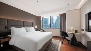 Habitación de hotel con una cama grande, un escritorio y una silla. Se ve una ventana con vista a la ciudad.