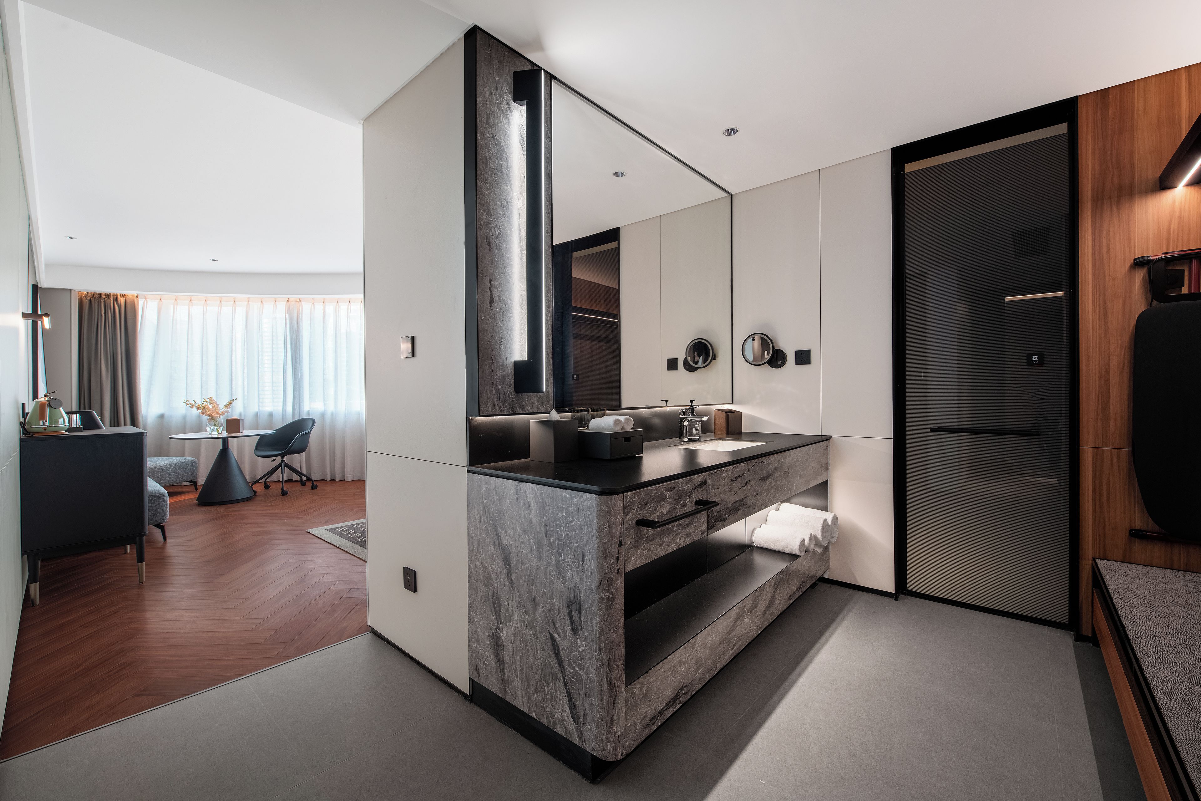 A modern bathroom with a large mirror, a dark countertop, and a wooden door.