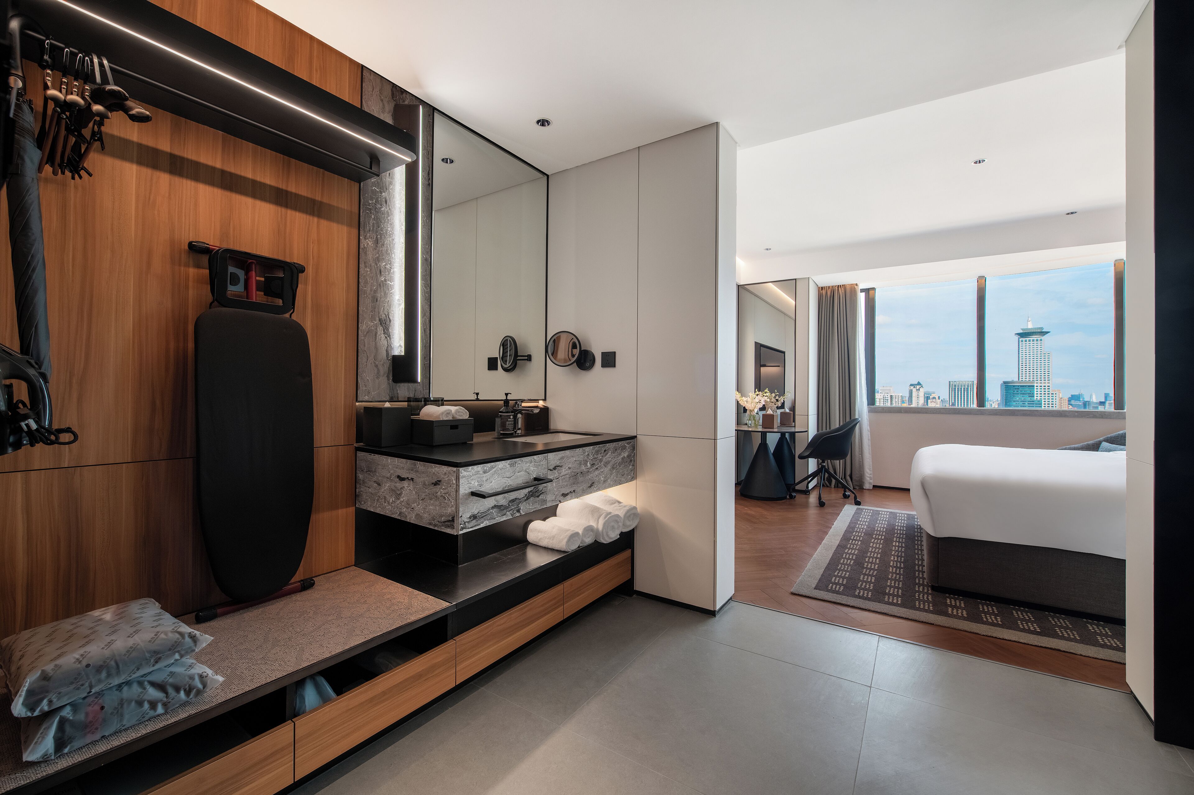 Una habitación de hotel moderna con una cama grande, un baño con tocador y vistas a la ciudad.