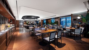Un restaurante moderno con barra central, varias mesas para comer y vistas de la ciudad a través de amplias ventanas.