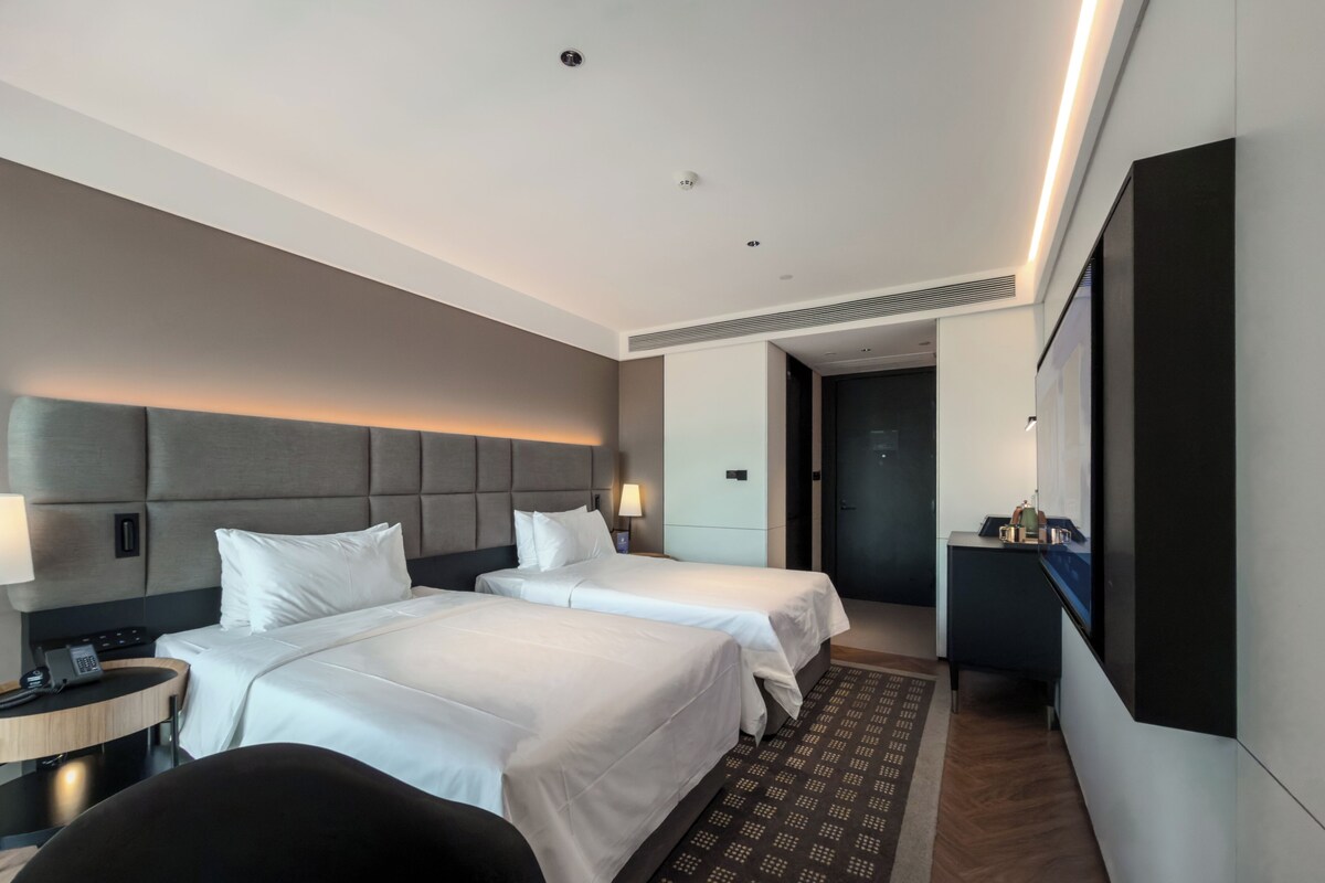 Ein Hotelzimmer mit zwei Betten, einem Schreibtisch, einem Stuhl, einem Fernseher und einer Badezimmertür.