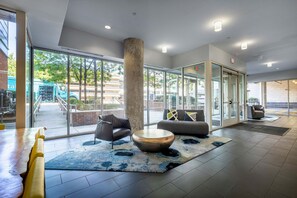 Eine moderne Lobby mit einer großen Glasdoor, einer zentralen Säule und einer Sitzecke mit rundem Tisch und Sofas.