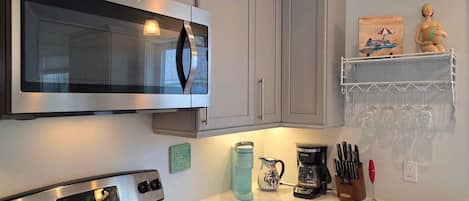 A kitchen with a microwave, stove, coffee maker, and a shelf with wine glasses.