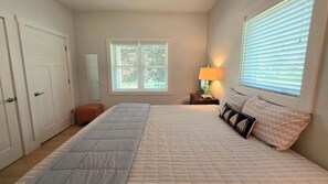 A bedroom with a bed, a nightstand, a lamp, a window with blinds, and a door. - Downtown Harbor Springs cottage with 4 bedrooms, 2 baths, yard, and grill. (Harbor Springs)