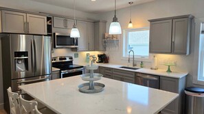 A modern kitchen with stainless steel appliances, a central island, pendant lighting, and a window providing natural light. - Downtown Harbor Springs cottage with 4 bedrooms, 2 baths, yard, and grill. (Harbor Springs)