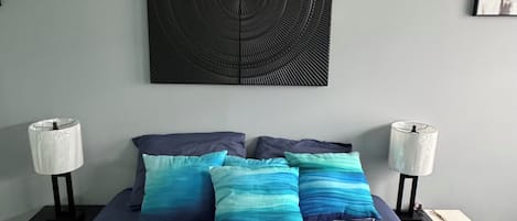 A bedroom with a bed, two bedside tables, a wall-mounted artwork, and a nightstand with a lamp.