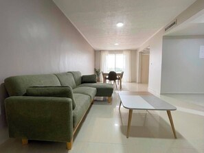 A modern living room with a sectional sofa, a dining table with chairs, and a large window providing natural light. - Minimalist & Calm: 5 Min away from La Vela Mall (Porlamar)