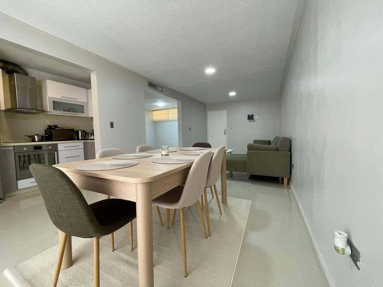 A modern kitchen with built-in appliances, a dining area with a wooden table and chairs, and a green sofa in the living area.