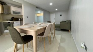 Une cuisine moderne dotée d’appareils électroménagers intégrés, un coin repas avec une table et des chaises en bois, et un canapé vert dans l’espace salon.