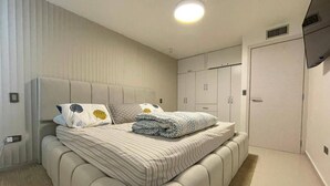 Une chambre moderne avec un grand lit, une armoire et un téléviseur fixé au mur.