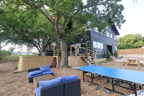 En udendørs patio med et ping pong bord, siddepladser og en træterrasse.