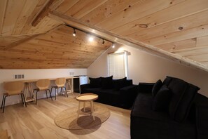 Un espai vital d'estil loft amb sostre inclinat, un sofà negre, una taula de centre rodona i un petit televisor.