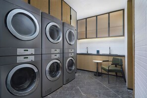A laundry area with multiple washing machines, a small sink, and a chair. - Four Points By Sheraton Fuzhou Changle (Fuzhou)
