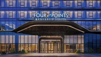 A hotel entrance with a modern design, featuring a glass facade and a sign that reads 'FOUR POINTS BY SHERATON'.
