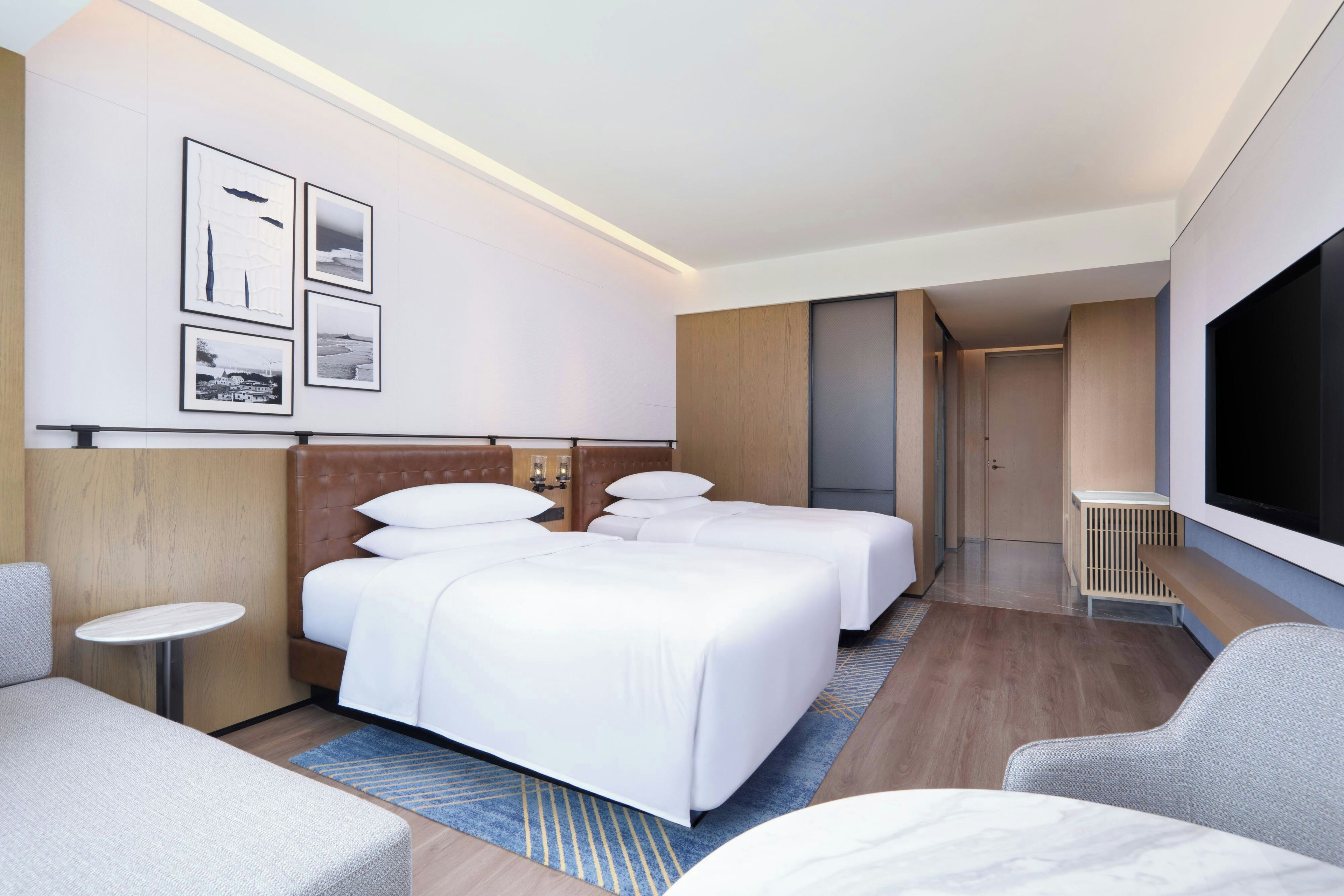 A hotel room with two beds, a TV, a small table, and a seating area.
