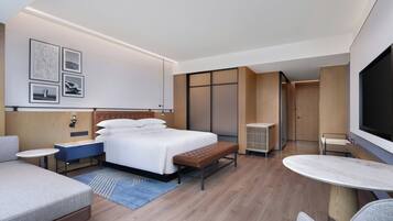 A modern hotel room with a bed, a seating area, a TV, and artwork on the wall.