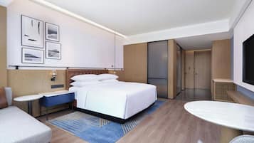 A modern hotel room with a large bed, a desk, a seating area, and a television.