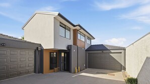 A modern two-story house with a garage, a covered driveway, and a small outdoor seating area. - Domi Rentals - The Ormond House (Clayton)