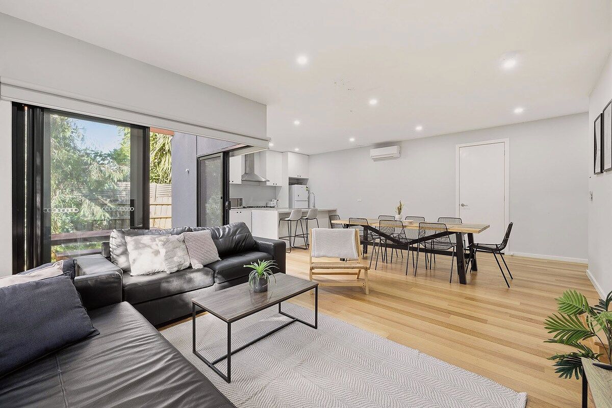 A modern living space with a sofa, coffee table, dining area, and kitchen.