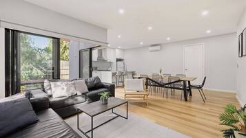 A modern living space with a sofa, coffee table, dining area, and kitchen.