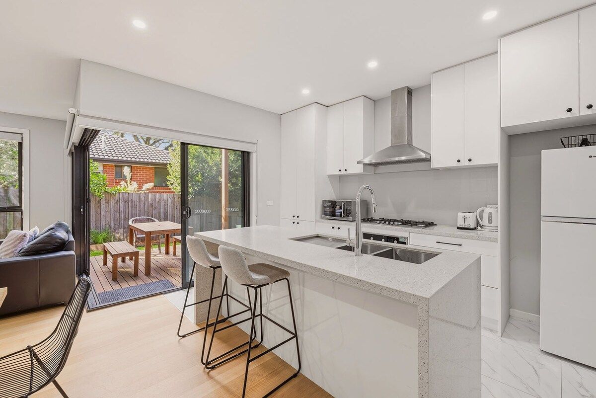 A modern kitchen with a central island, white cabinetry, and a view to a backyard patio.