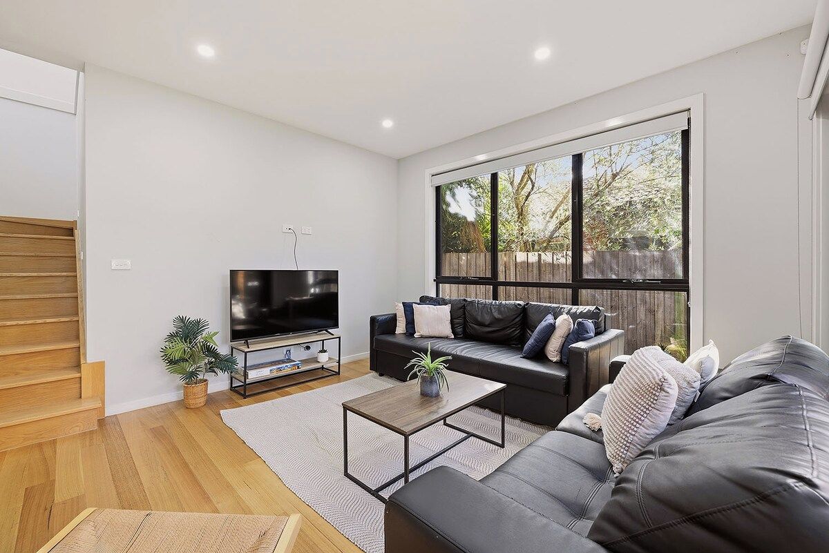 A modern living room with a flat-screen TV, a sofa, a coffee table, and a staircase.