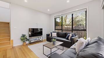 A modern living room with a flat-screen TV, a sofa, a coffee table, and a staircase.